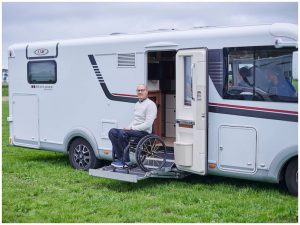 Man in handbewogen rolstoel kom aan de zijkant van een camper met een liftje naar beneden