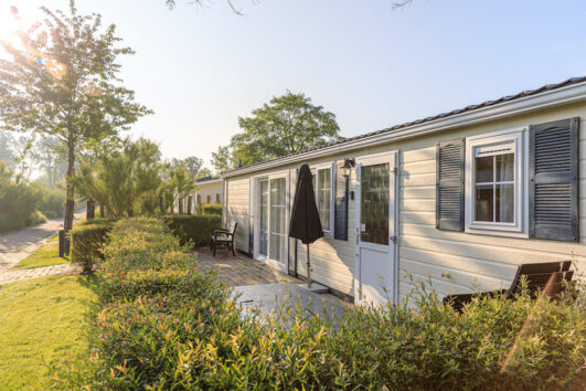 wit chalet met blauwe luikjes en een groene heg ervoor