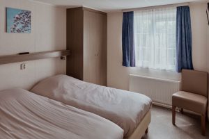 twee bedden naast elkaar met een raam en blauwe gordijnen