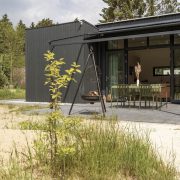 Zwart houten huisje met grote raampartij bij terras met tafel, vuurschaal en hottub