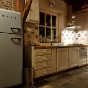 Keuken in het huisje, met raam boven het aanrecht, zichtbaar is oa de Smeg koelkast met vriesgedeelte boven. Een oven onder het fornuis met vier gaspitten