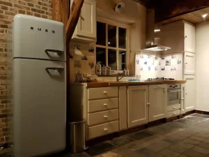 Keuken in het huisje, met raam boven het aanrecht, zichtbaar is oa de Smeg koelkast met vriesgedeelte boven. Een oven onder het fornuis met vier gaspitten