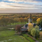 luchtfoto met een molen en een paar gebouwen waaronder de Wachtershof daaromheen bomen in herfstkleuren