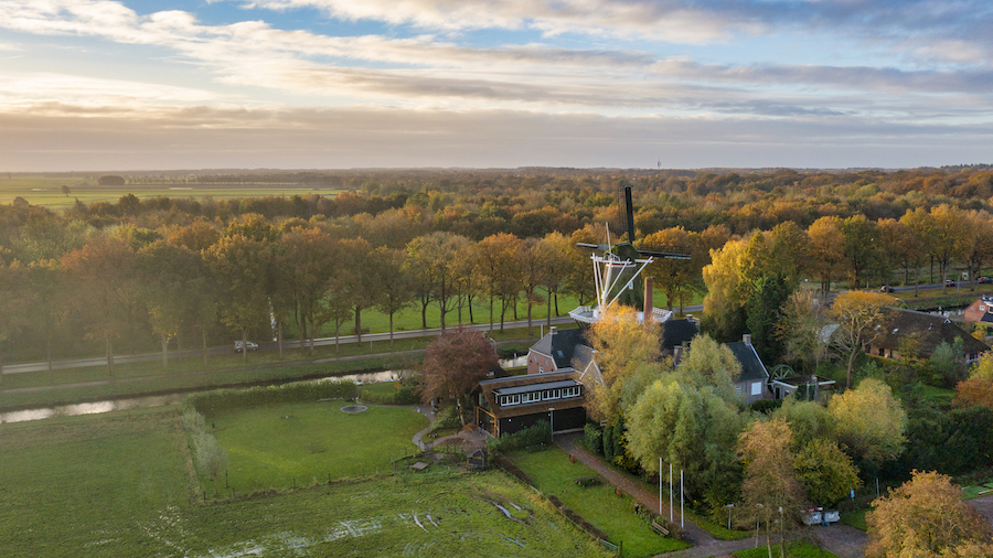 luchtfoto met een molen en een paar gebouwen waaronder de Wachtershof daaromheen bomen in herfstkleuren