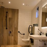 Het Gouwe Boetje, badkamer douchehoek met zwart Linido douchezitje en houtkleurige wandtegels en regendouche