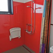badkamer met knalrode muren, douchehoek met verstelbare glijstang en opgeklapt douchestoeltje aan de wand (zonder armleuningen), geen drempels op de vloer
