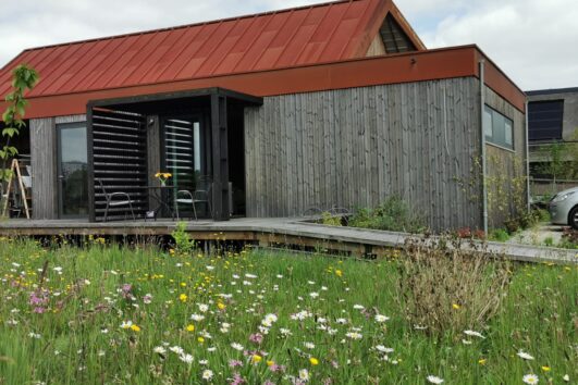Houten huis met rood dak en houten vlonder met schuine helling naar de deur