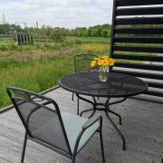 Houten vlonderterras met (zwart ijzeren) tafeltje en 2 stoelen en prachtig vrij uitzicht over bloemenvelden