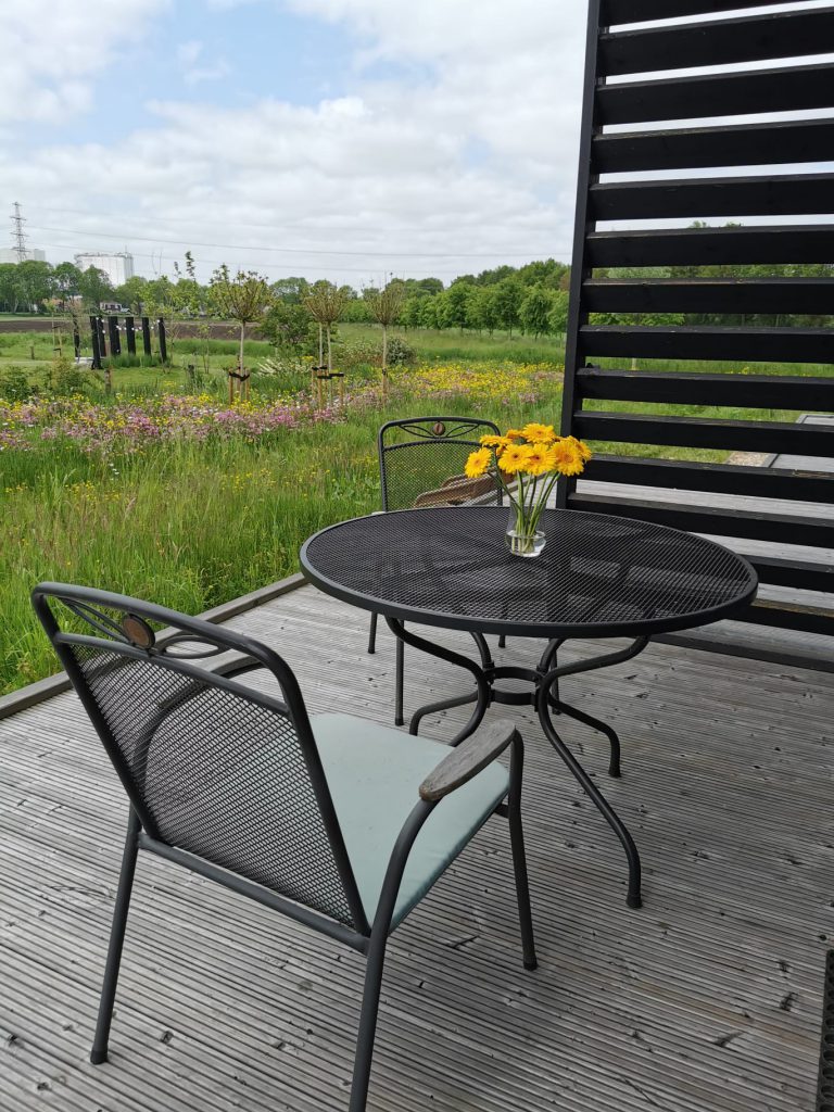 Houten vlonderterras met (zwart ijzeren) tafeltje en 2 stoelen en prachtig vrij uitzicht over bloemenvelden