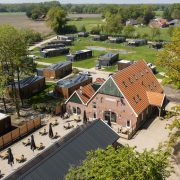 droge beeld van het park met huisjes rondom een 8-vormige vijver en boerderij met terras en tafeltjes (het restaurant)