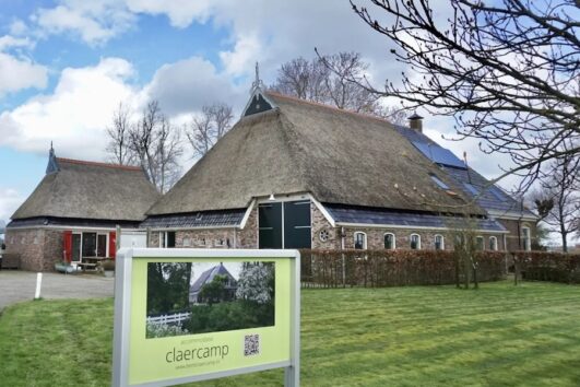 Rietgekapte grote boerderij in grasveld met een een aangebouwde kleinere 'stal'
