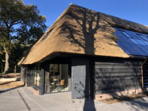 Zwart houten schuur met rietkap en glazen wand met deur