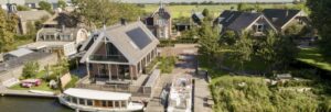 luchtfoto van het huis. De potonboot van Stichting Vaarervaaring ligt rechts in het water, voor het huis aan een steiger