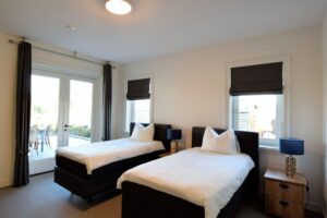 slaapkamer beneden met twee losstaande boxspringbedden, twee ramen en openslaande deuren