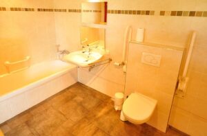 Badkamer met bad (vrij lage instap), onderrijdbare wastafel, met twee spiegels boven elkaar, toilet met opklapbare beugels